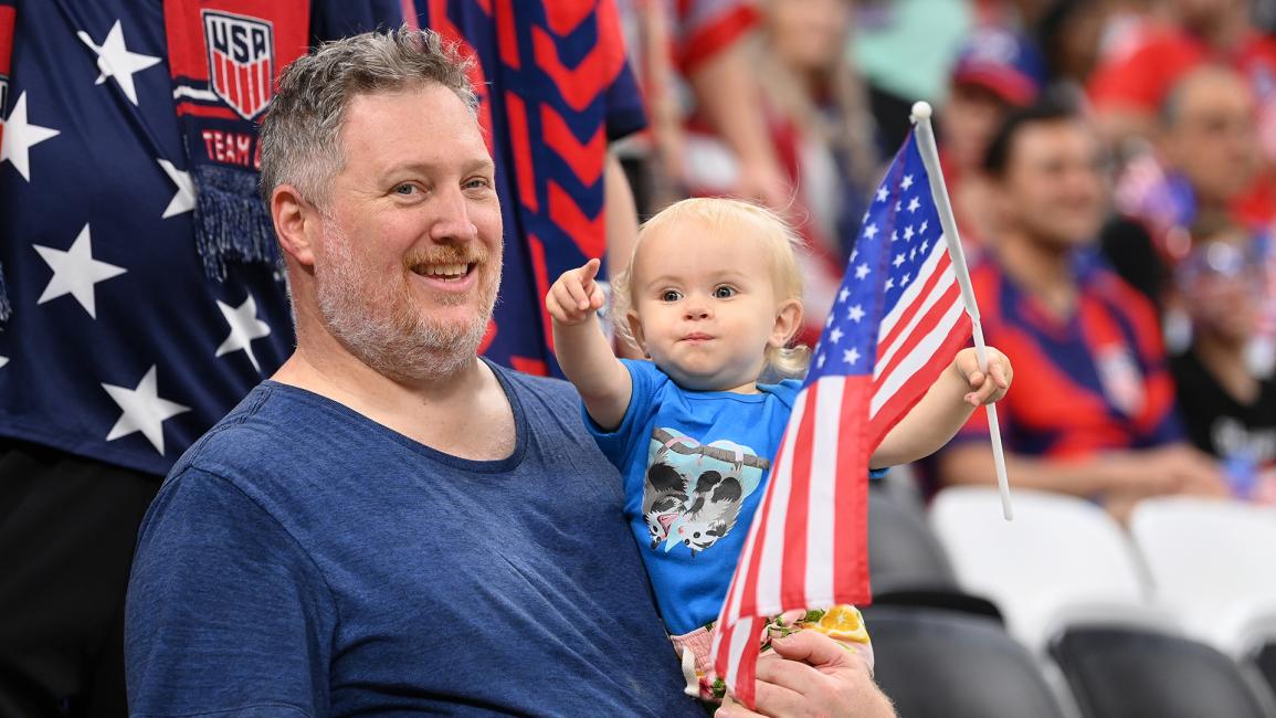 مشجع أميركي يحمل رضيعاً أثناء مباراة إنكلترا والولايات المتحدة (ستو فورستر/Getty)