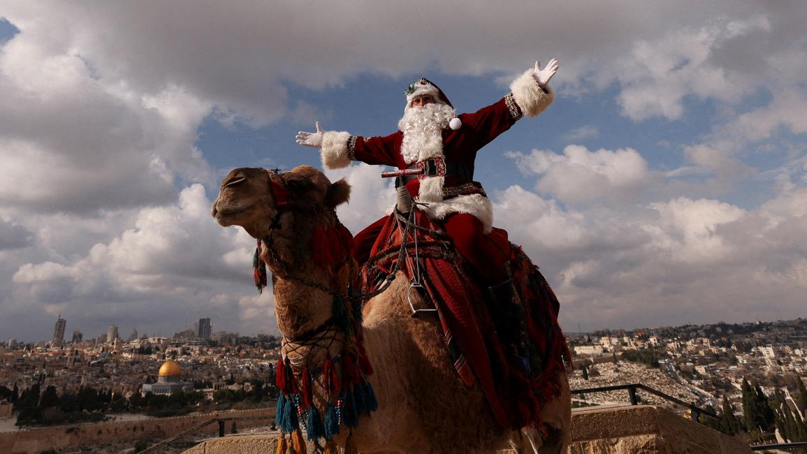 بابا نويل على ناقة خلال موسم عيد الميلاد على جبل الزيتون في القدس، وخلفه قبة الصخرة (عمار عوض/رويترز)