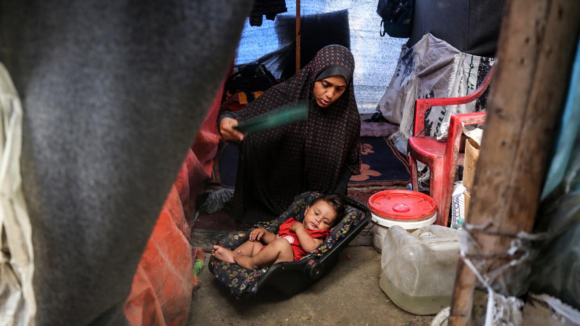 فلسطينية تستخدم طبقاً بلاستيكياً لتهوية طفلها خلال موجة الحر (مجدي فتحي/Getty)