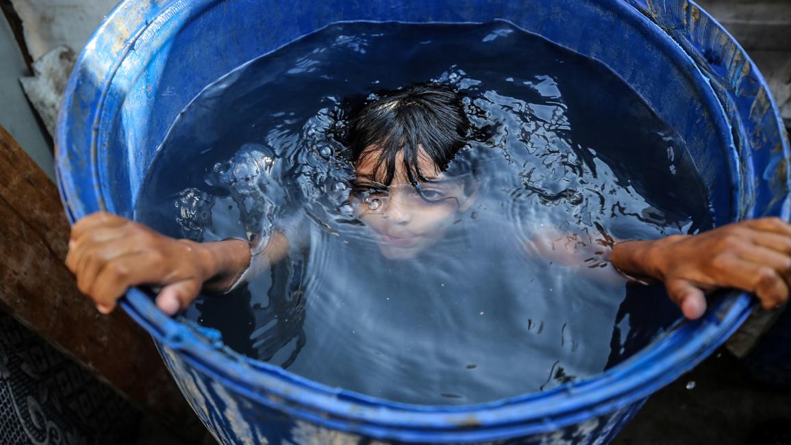 صبي فلسطيني يغتسل بالماء أمام خيمته لخفض درجات الحرارة (مجدي فتحي/Getty)