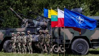 جنود بولنديون ورومانيون يقفون بجوار علم الناتو في قرية شيبليسكي، 7 يوليو 2022 (فرانس برس)