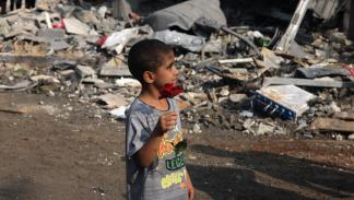 طفل فلسطيني يحمل وردة وسط الدمار الذي سببته الغارات الإسرائيلية، غزّة، 2023 (Getty)