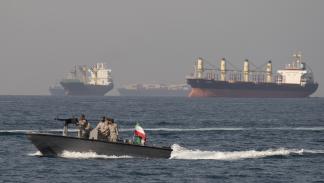 سفن تحمل شحنات نفط وسلعاً بالقرب من مضيق هرمز، خلف زورق عسكري إيراني (مرتضى نيكوبازل/Getty)