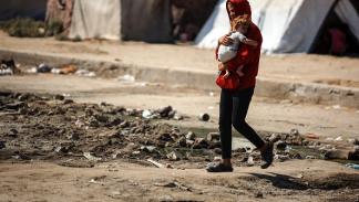 فتى يحمل طفلة خلال رحلة النزوح المتكررة في قطاع غزة / 22 يوليو 2024 (Getty)