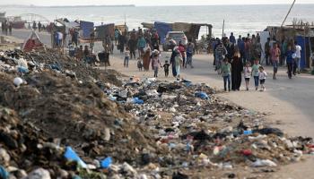 فلسطينيون يسيرون بجوار أكوام القمامة في دير البلح، 26 مايو 2024 (الأناضول)