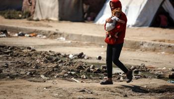 فتى يحمل طفلة خلال رحلة النزوح المتكررة في قطاع غزة / 22 يوليو 2024 (Getty)