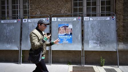 يعبر أمام ملصق انتخابي لمارين لوبان في باريس، 23 يونيو 2024 (ريمون هازن/ Getty)