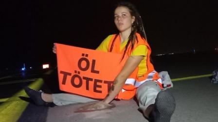 ناشطة مناخ تحمل لافتة "النفط يقتل" بمطار لايبزيغ - هاله بشرق ألمانيا، 1 أغسطس 2024 (إكس)