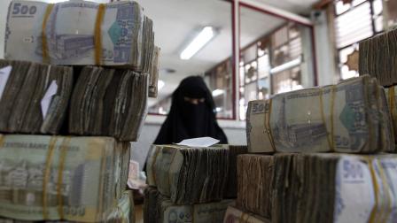 موظفة أمام رزم من الريالات في البنك المركزي اليمني (محمد حويس/فرانس برس)